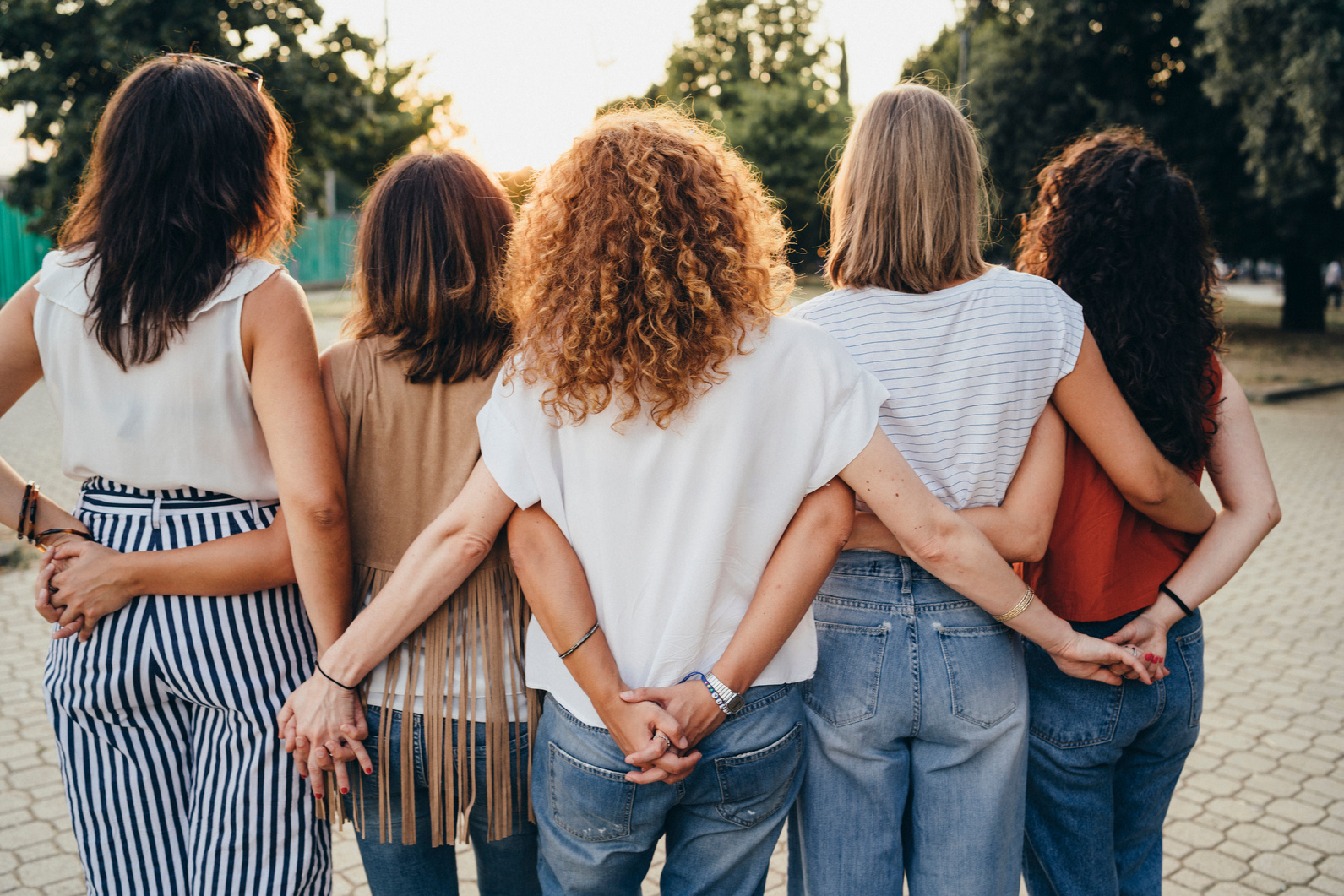 Group of women friends holding hands together against sunset